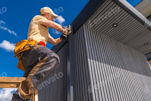 Preview: Worker on ladder installing panels on a building under clear blue sky
