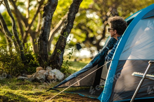 Preview: Person sitting outside tent during camping in nature at sunny day