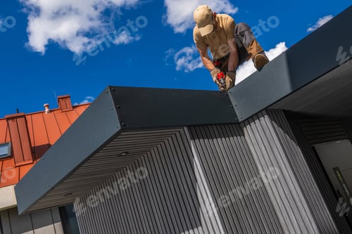 Preview: Worker performs construction task on roof in bright blue sky