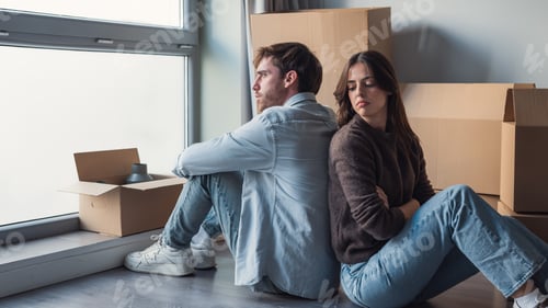 Preview: Couple sitting back to back amid moving boxes looking upset during a stressful moving day