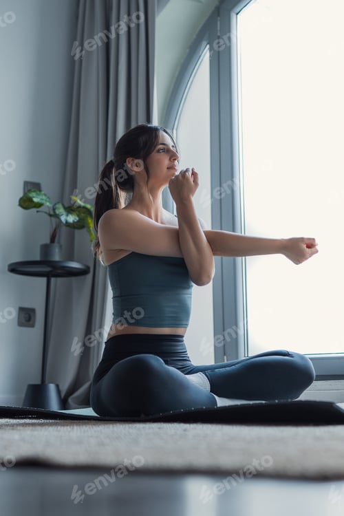 Preview: Young woman stretching in seated yoga pose during a calm home workout by a bright window