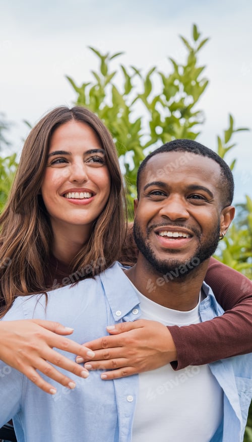 Preview: Smiling mixed-race couple enjoying a joyful outdoor moment together in a natural green setting