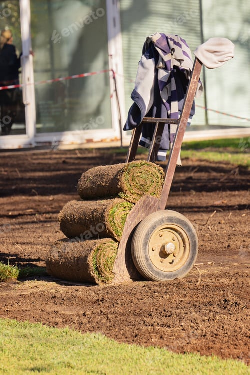 Preview: Turf rolls on hand dolly at landscaping work site with dark tilled soil
