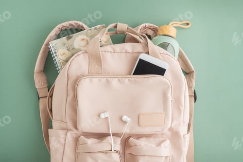 Preview: Backpack with notebook, phone, bottle, and earphones on green background