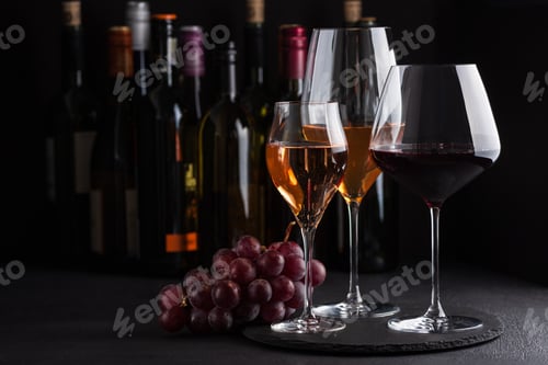 Preview: Three glasses of red, white and sparkling rose wine with bunch of grapes on dark slate background