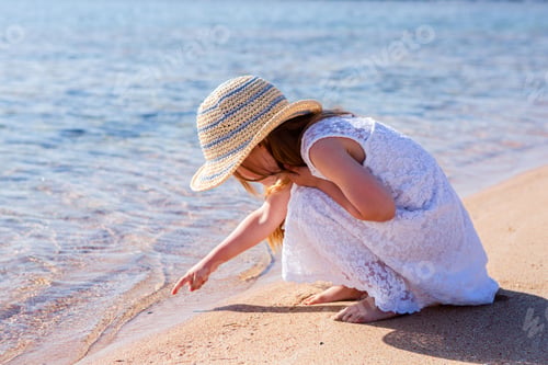 Preview: Little girl in white dress playing on sunny beach with straw hat and ocean pier