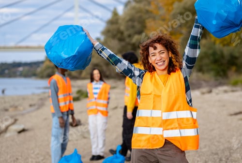 Preview: Portrait of smiling female volunteer in a safety vest holding trash bags during a community environm