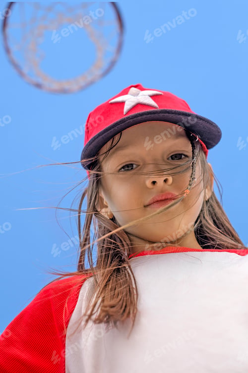 Preview: Portrait of a cute girl in a sports cap against the sky and a basketball basket