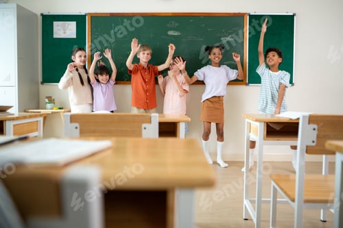 Preview: Diverse group of school children raising hands happily in classroom