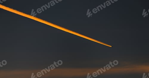 Preview: Golden airplane contrail across the sunset sky with a dark cloud background