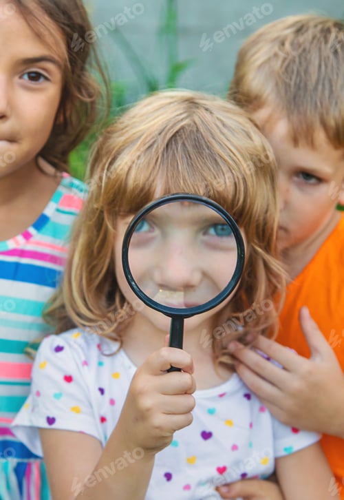 Preview: Children look at a magnifying glass on the nature. Selective focus.