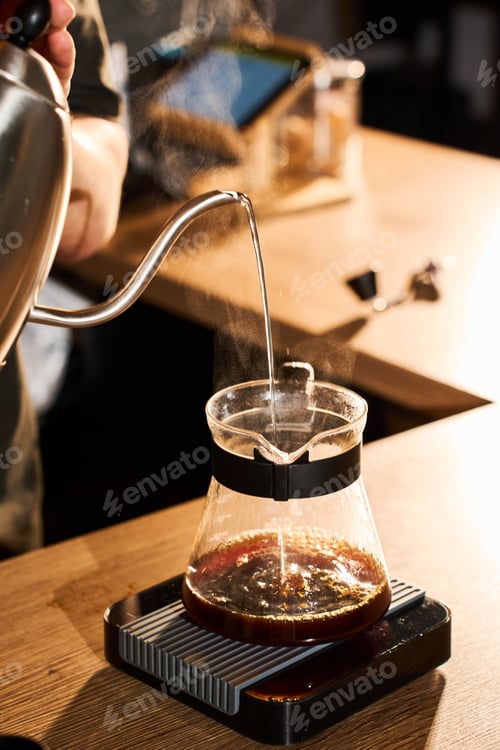 Preview: Barista pouring hot water from a gooseneck kettle to dilute AeroPress coffee concentrate.