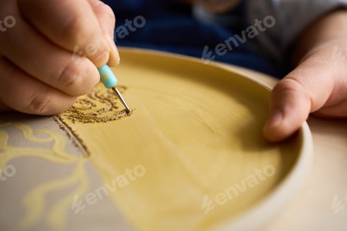Preview: Artisan crafting complex geometric patterns on a ceramic platter using a fine engraving loop.