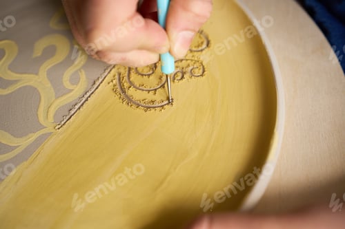 Preview: Close up photography of texture being carved into a dried clay plate in a studio.