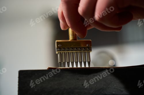 Preview: Artisan hands using a heavy mallet and a brass stitching punch to make holes in leather.