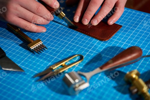 Preview: Artisan finishing leather edges with a specialized wooden-handled tool on a blue cutting mat.