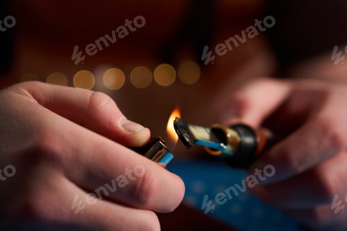 Preview: Leathercrafter in an apron using a lighter to heat a metal edge creaser over a blue mat.
