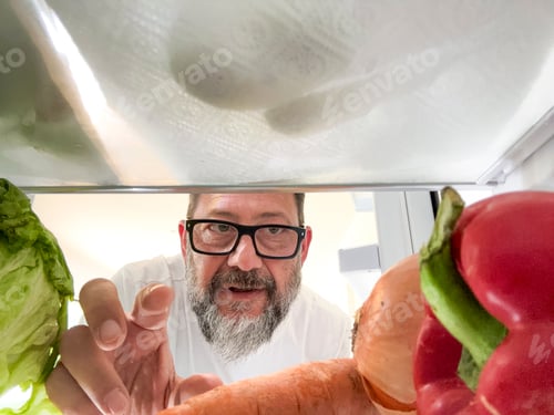 Preview: Man with glasses and beard reaches into open fridge from pov, selecting fresh colorful vegetables fo