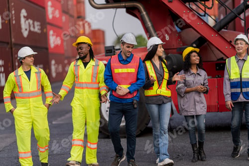 Preview: Team logistics workers in high visibility safety gear and hard hats discuss operations at a busy shi