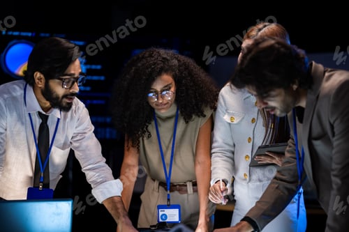 Preview: Male tech presenter in a tan blazer addresses a diverse team in a dark briefing room with blue AI ca