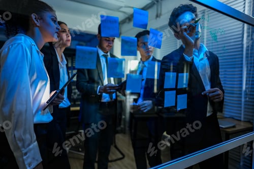 Preview: High energy team strategy meeting in a modern office at night. Business professionals using sticky n
