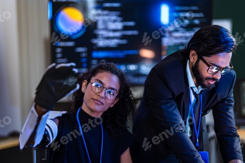 Preview: Black female tech innovator wearing a white bionic arm and South Asian male security professional re