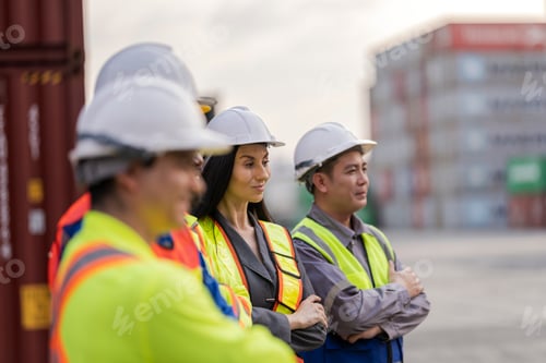 Preview: Team logistics workers in high visibility safety gear and hard hats discuss operations at a busy shi