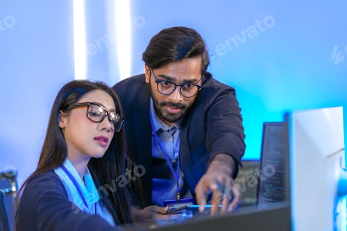 Preview: Two software developers wearing glasses and ID lanyards talking through the program logic together,
