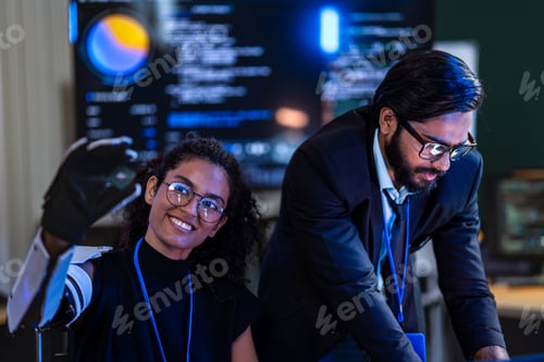 Preview: Black female cybersecurity engineer with a white robotic arm and South Asian male analyst examine in