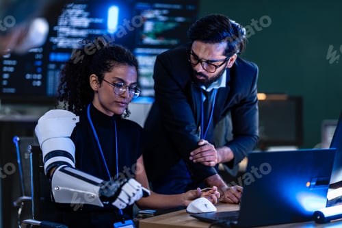 Preview: South Asian male IT security analyst and Black female engineer with a bionic arm collaborate in a da