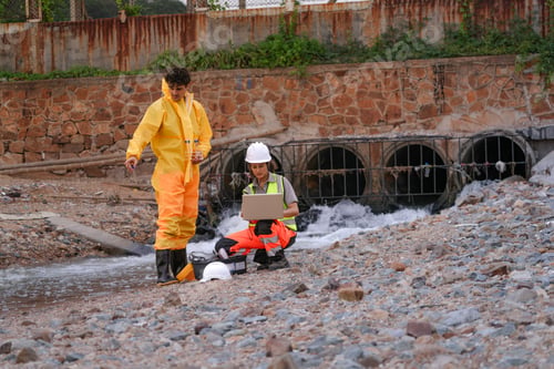 Preview: Environmental field team in protective gear analyzes water samples on a polluted beach. One holds a