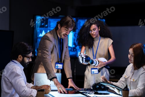 Preview: Caucasian male in a tan blazer addresses a seated diverse tech team in a dark briefing room with blu