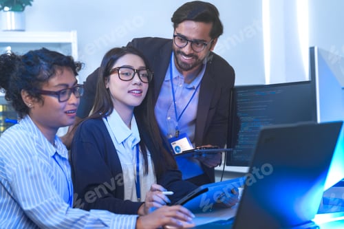Preview: Two engineers seen from behind studying source code on large monitors, facing a wall of monitors fil