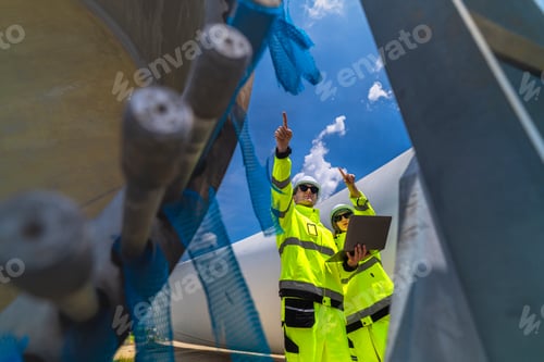 Preview: Two engineers in safety gear inspecting a wind turbine blade section on a construction site. They ex