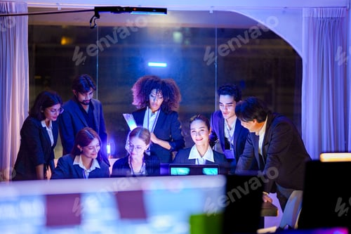 Preview: A large, diverse team of young business professionals smiling and collaborating during a night sessi