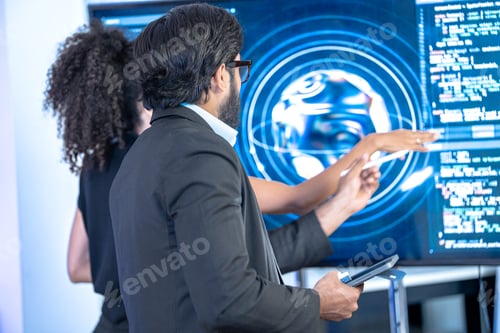 Preview: South Asian male and Black female developers review AI hologram displays on a large wall screen in a