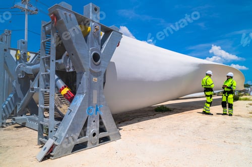 Preview: Wind turbine engineers standing by a large turbine blade at a renewable energy facility, overseeing