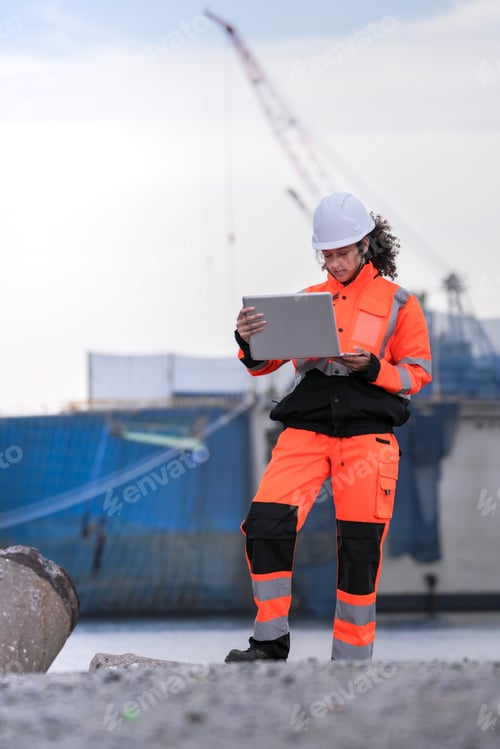 Preview: Diverse industrial engineers in orange safety uniforms and hard hats collaborating with a laptop at