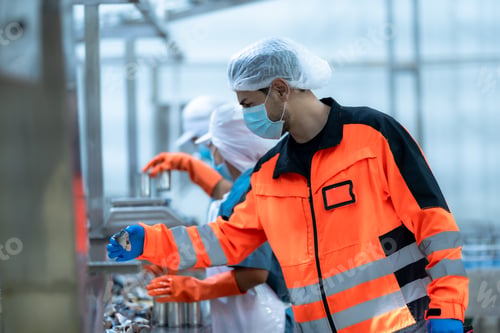 Preview: Two food safety experts in protective gear inspecting canned products on a production line while rec