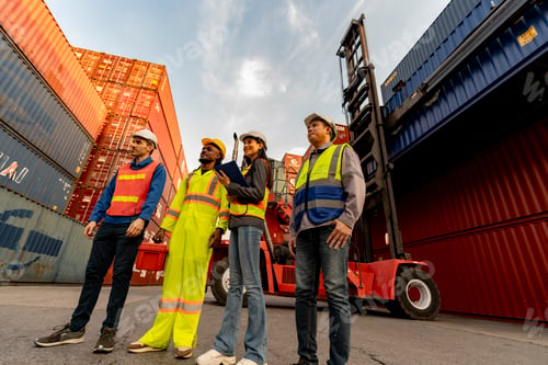Preview: Happy diverse logistics team celebrating success by raising fists together at a container port. Succ