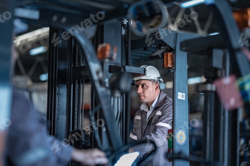 Preview: Caucasian male factory supervisor talking on radio with forklift driver in foreground. Industrial lo