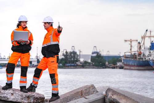Preview: Two port engineers in high-visibility orange uniforms and hard hats communicate while inspecting doc