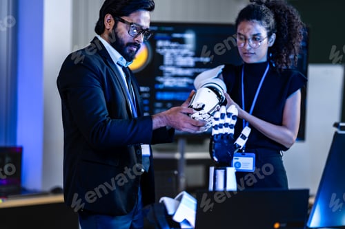 Preview: South Asian male IT professional and Black female specialist with a white robotic arm review a cyber