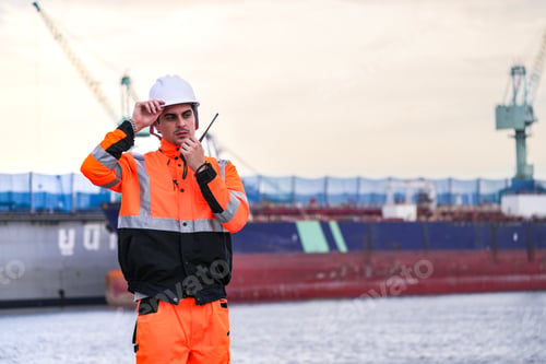 Preview: Two port engineers in high-visibility orange uniforms and hard hats communicate while inspecting doc