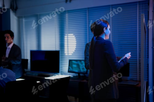 Preview: Back view of a female developer with curly hair stretching her neck while sitting at a desk in a dar