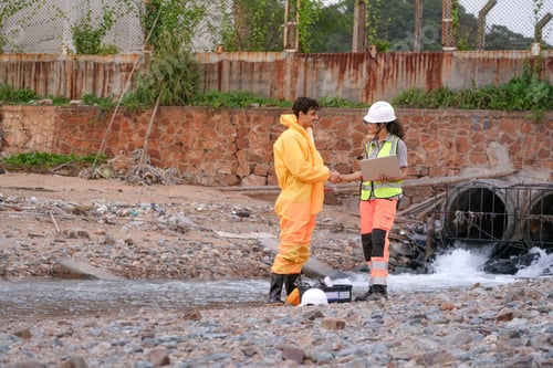 Preview: Environmental field team in protective gear analyzes water samples on a polluted beach. One holds a