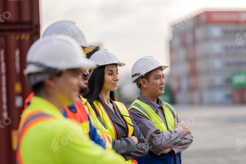 Preview: Team logistics workers in high visibility safety gear and hard hats discuss operations at a busy shi