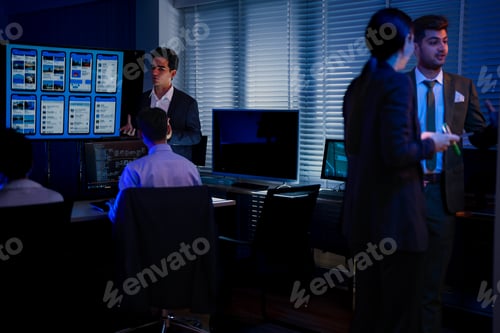 Preview: Back view of a female developer with curly hair stretching her neck while sitting at a desk in a dar