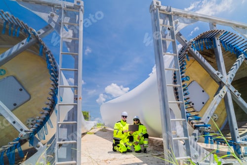 Preview: Two engineers in safety gear inspecting a wind turbine blade section on a construction site. They ex