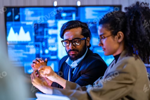 Preview: South Asian male and Black female cybersecurity professionals review digital forensics data in a blu